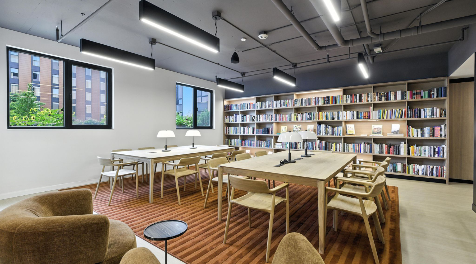 Contemporary reading room with stylish wooden tables, modern lighting, and extensive book collection against large windows offering urban views at Bakers Place in Madison